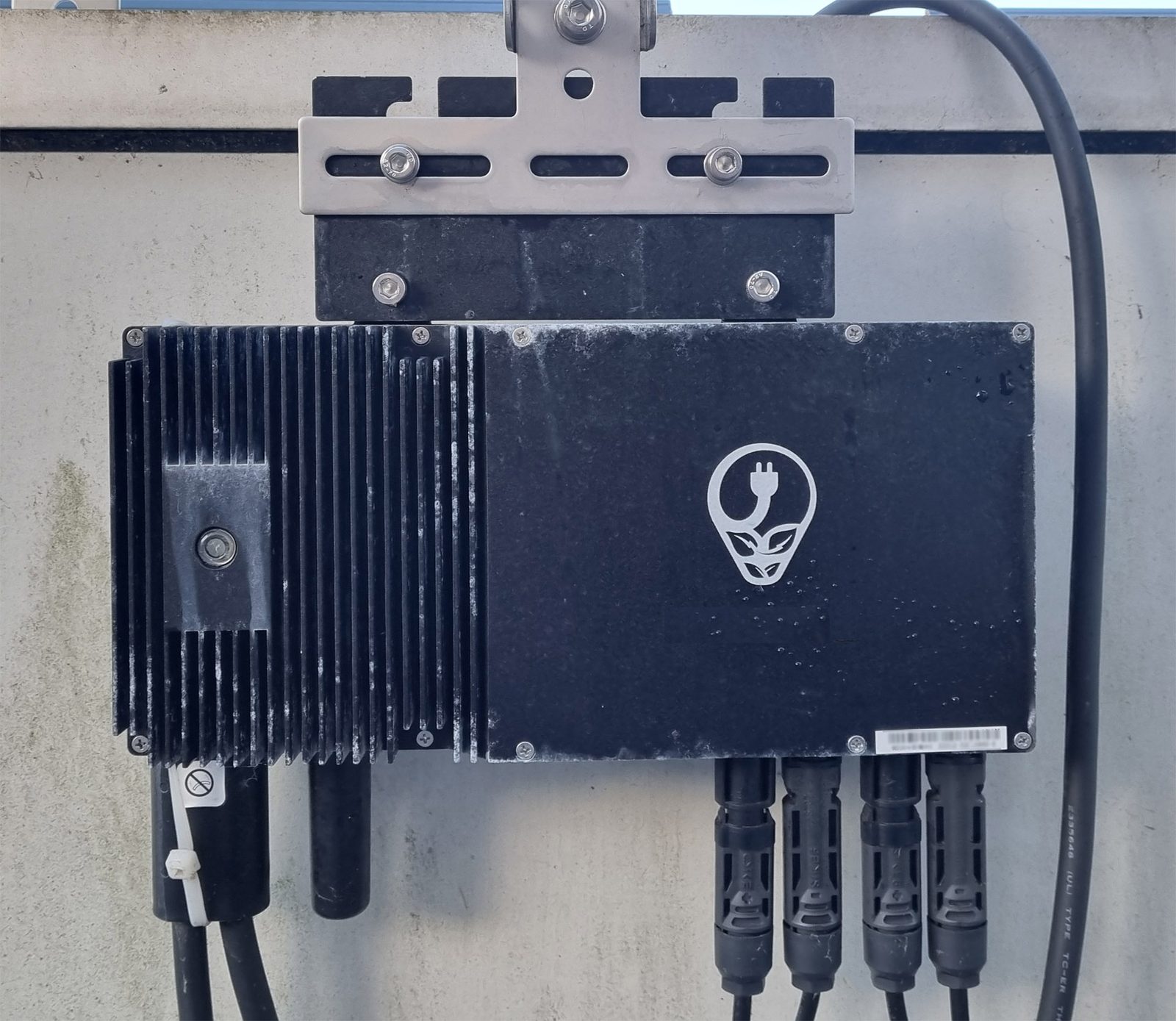 A solar micro-inverter mounted behind a balcony panel with DC connectors and an output cable